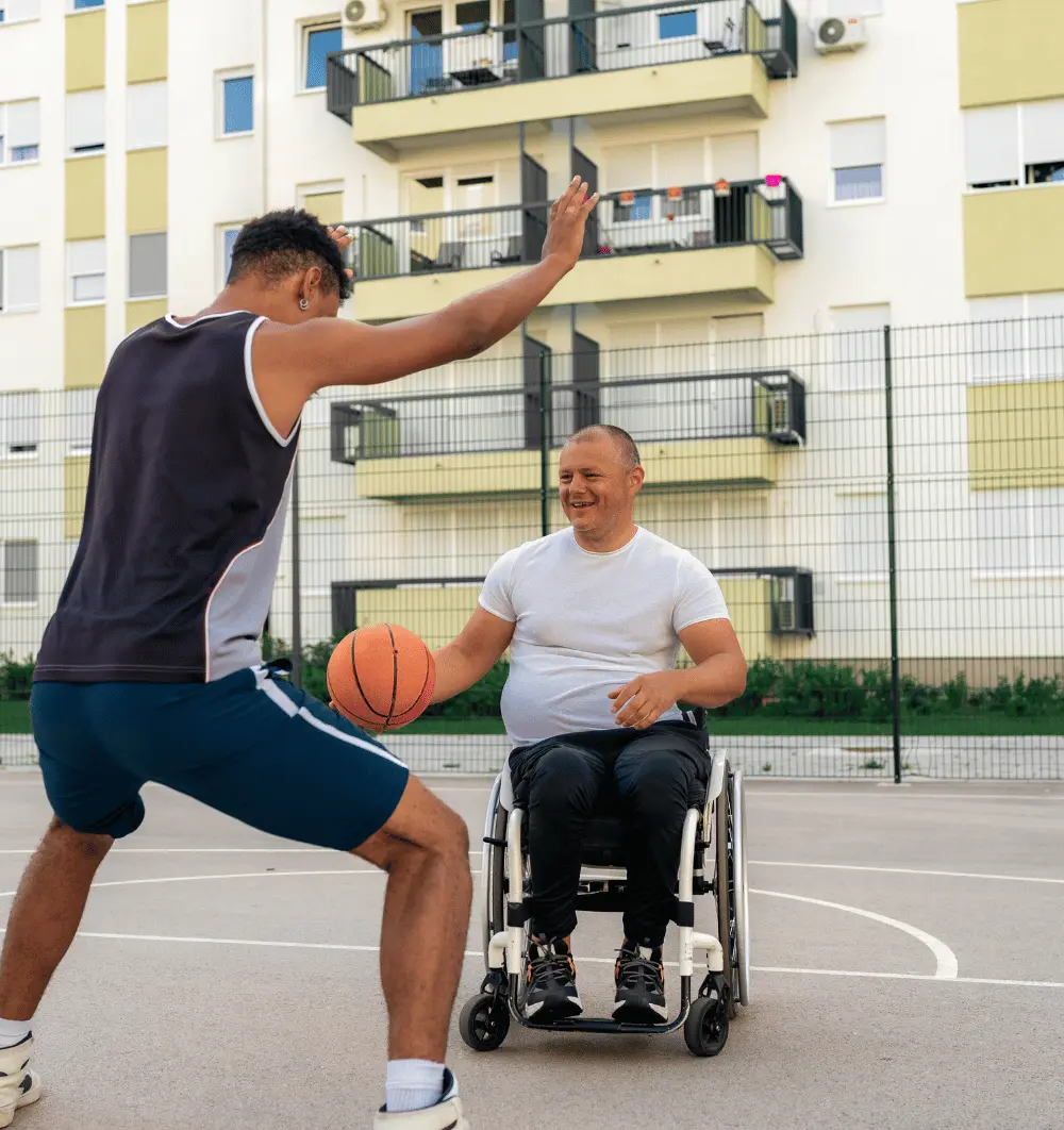 Disabled man in wheelchair playing basketball with a friend on outdoor basketball court