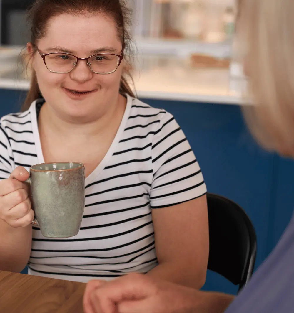 Happy disabled woman with down syndrome having a cup of tea with support worker