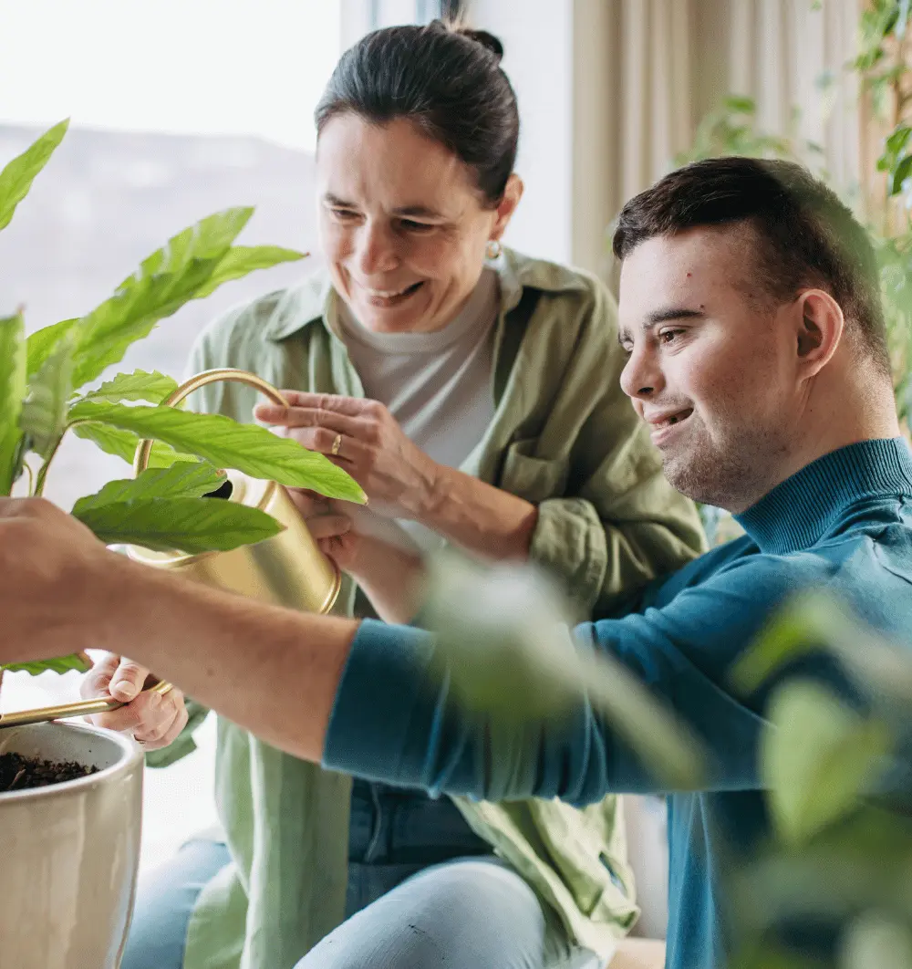 Disabled man with down syndrome tending to plants with support worker